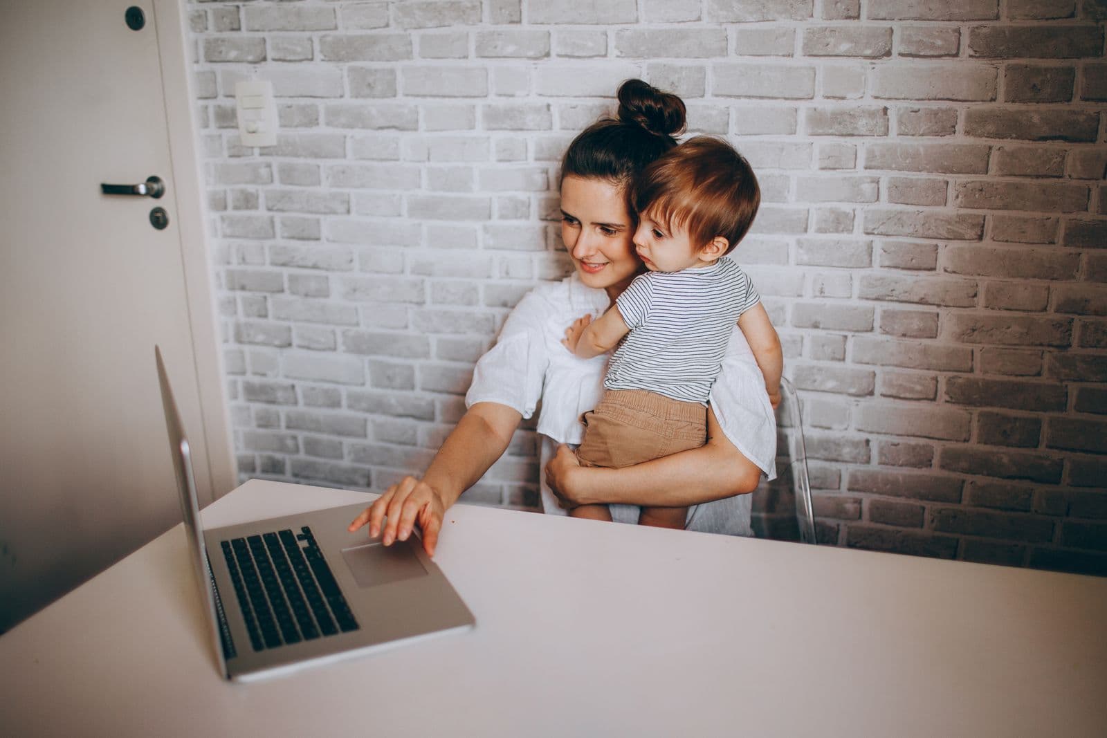 A mother working on a laptop while holding her toddler